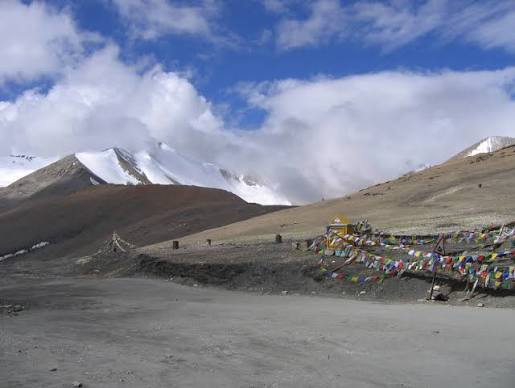 Khardung La high mountain pass with colorful Buddhist prayer flags fluttering under white clouds in August